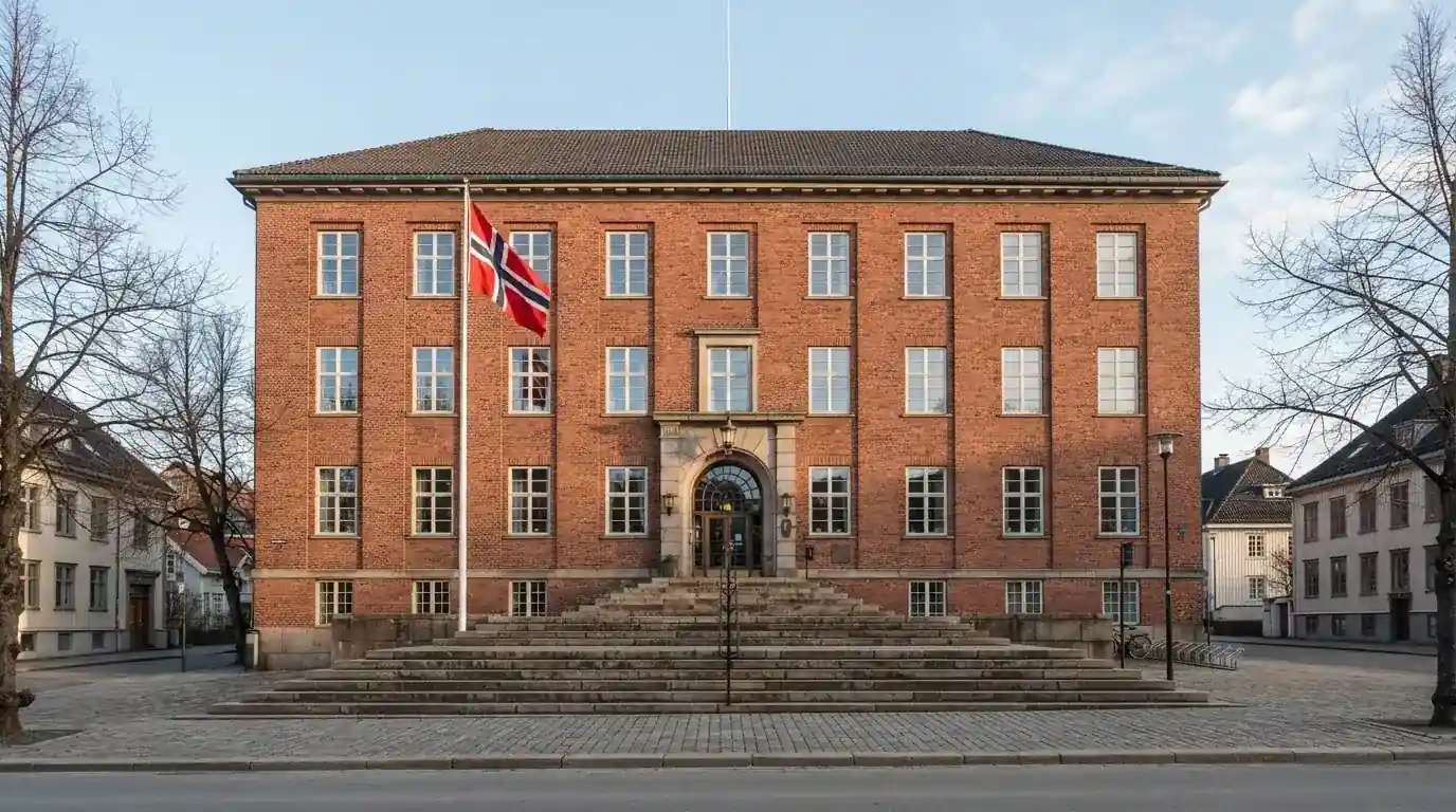 Offentlig kontorbygning i rødt murstein i en norsk by, med et flagg ved inngangen og blå himmel