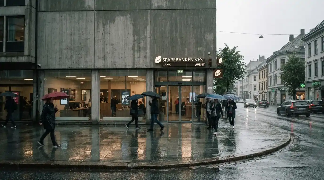 Bankfilial med store vinduer i en norsk by i regnvær, noen med paraplyer utenfor